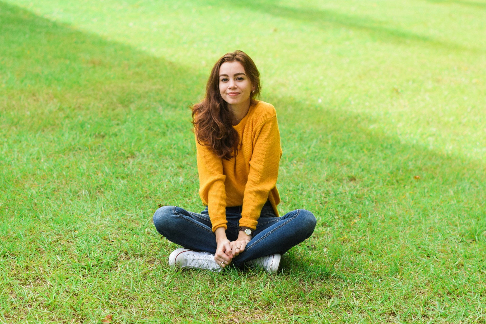 Sarah smiling in a yellow jumper sitting on grass