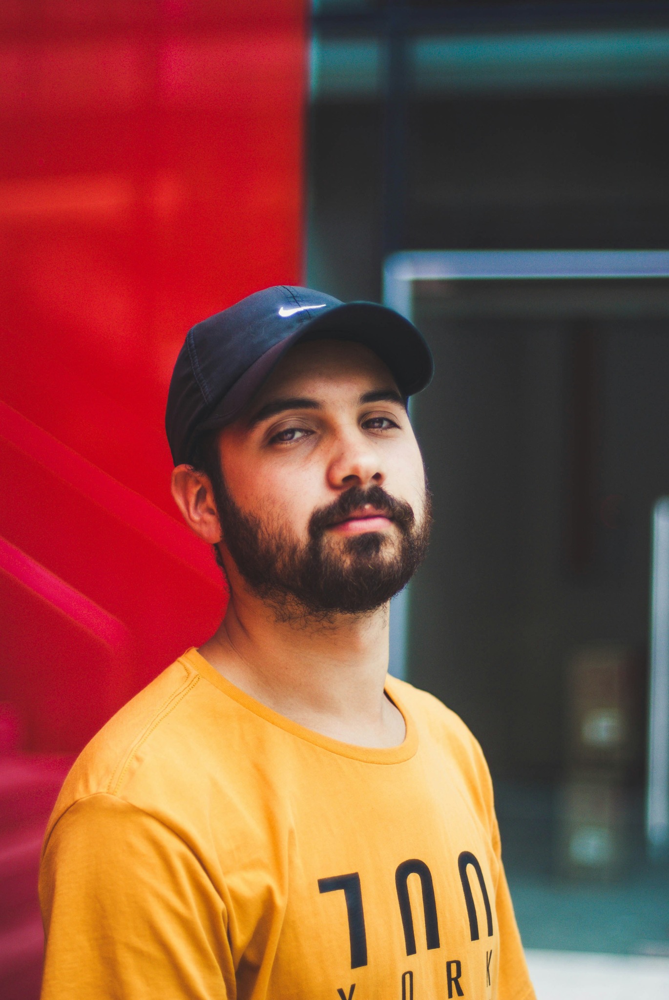 Luis wearing a cap and red shirt, smiling against a red wall